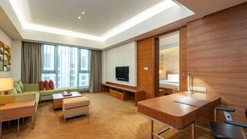 Quarto de hotel moderno com sofá, televisão, escrivaninha e uma janela grande com cortinas.