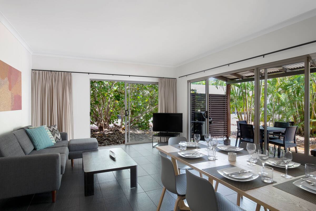 A modern living room with a sofa, a coffee table, and a dining area set for four.