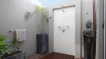 A small, enclosed shower area with a wooden floor, a towel hanging on a rack, a potted plant, and a statue.