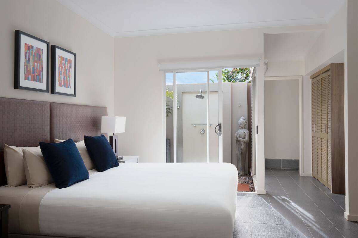 A modern hotel room with a large bed, a nightstand, a lamp, and a view of the outside.