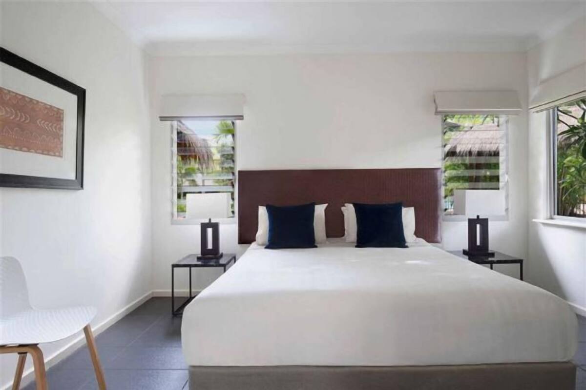 A hotel room with a large bed, two bedside tables, a chair, and a window with a view of palm trees.