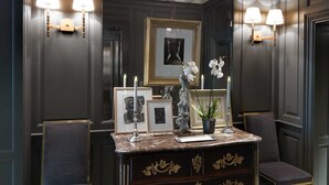 A dark wood-paneled room with a marble-top desk, two wall sconces, framed artwork, and a chair. - Marquis Faubourg Saint Honoré - Small Luxury hotels of the World (Paris)