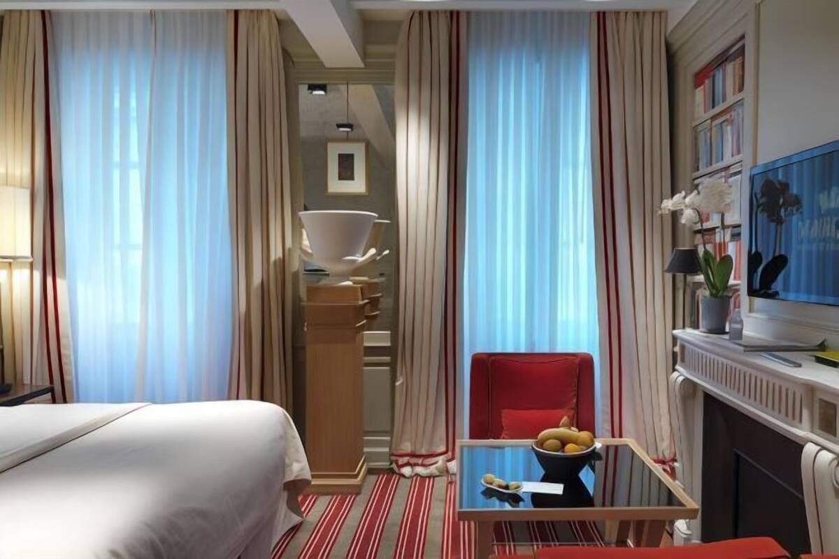 Une chambre d’hôtel avec un lit, une table à manger avec des fruits, une chaise rouge, une télévision et une cheminée.