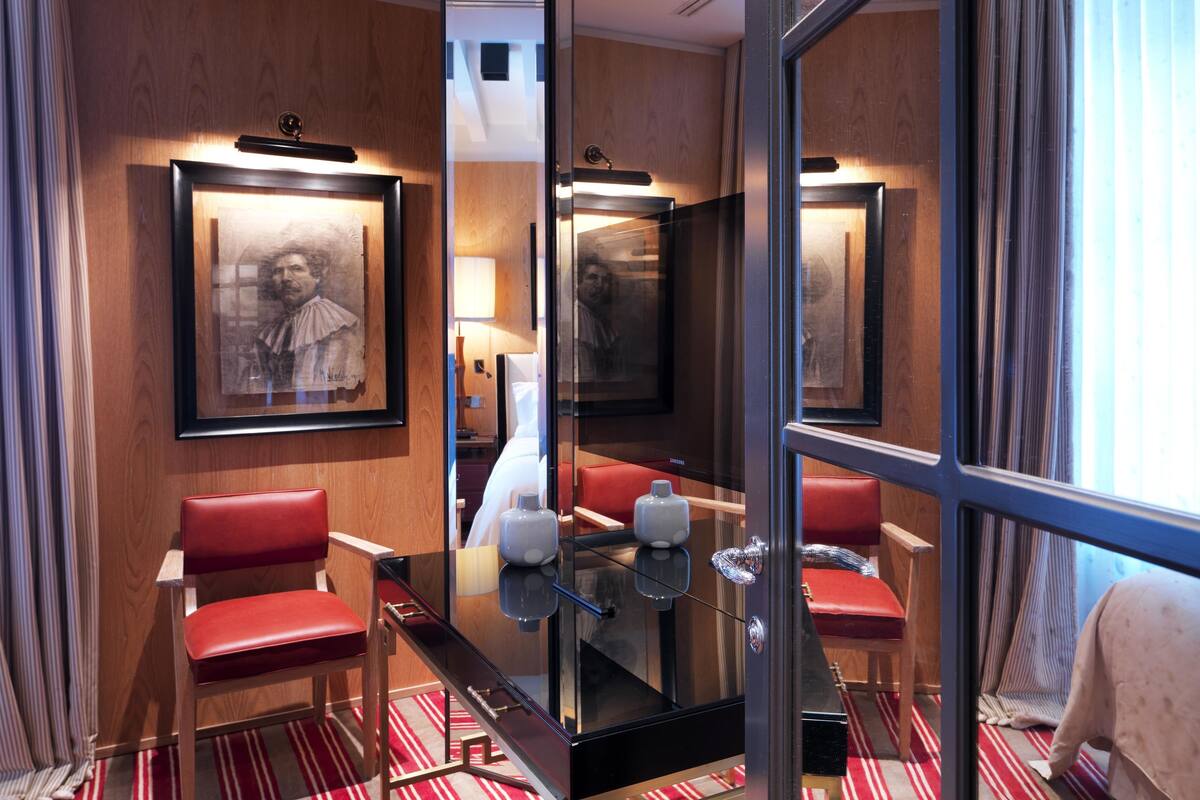 Une chambre d’hôtel avec un grand miroir, des fauteuils rouges, une table en verre et un tableau encadré accroché au mur.