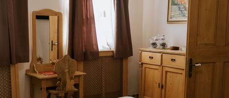A bedroom with a bed, wooden desk, chair, wardrobe, and a hanging light fixture.
