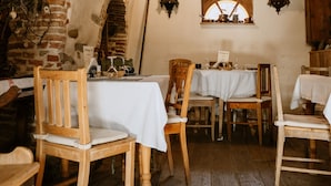 Comedor rústico con sillas y mesas de madera, pared de ladrillo y techo de madera.