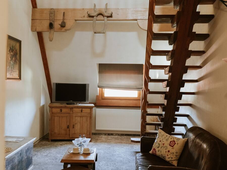 A cozy living room with a wooden staircase, a television, a wooden cabinet, and a leather sofa.