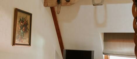 A rustic room with a wooden ceiling, a television on a wooden cabinet, a table with a teapot, and a vintage blue chest of drawers.