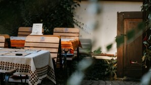 Un espacio de comedor al aire libre con mesas y sillas, una maceta colgante y una estructura de madera al fondo.