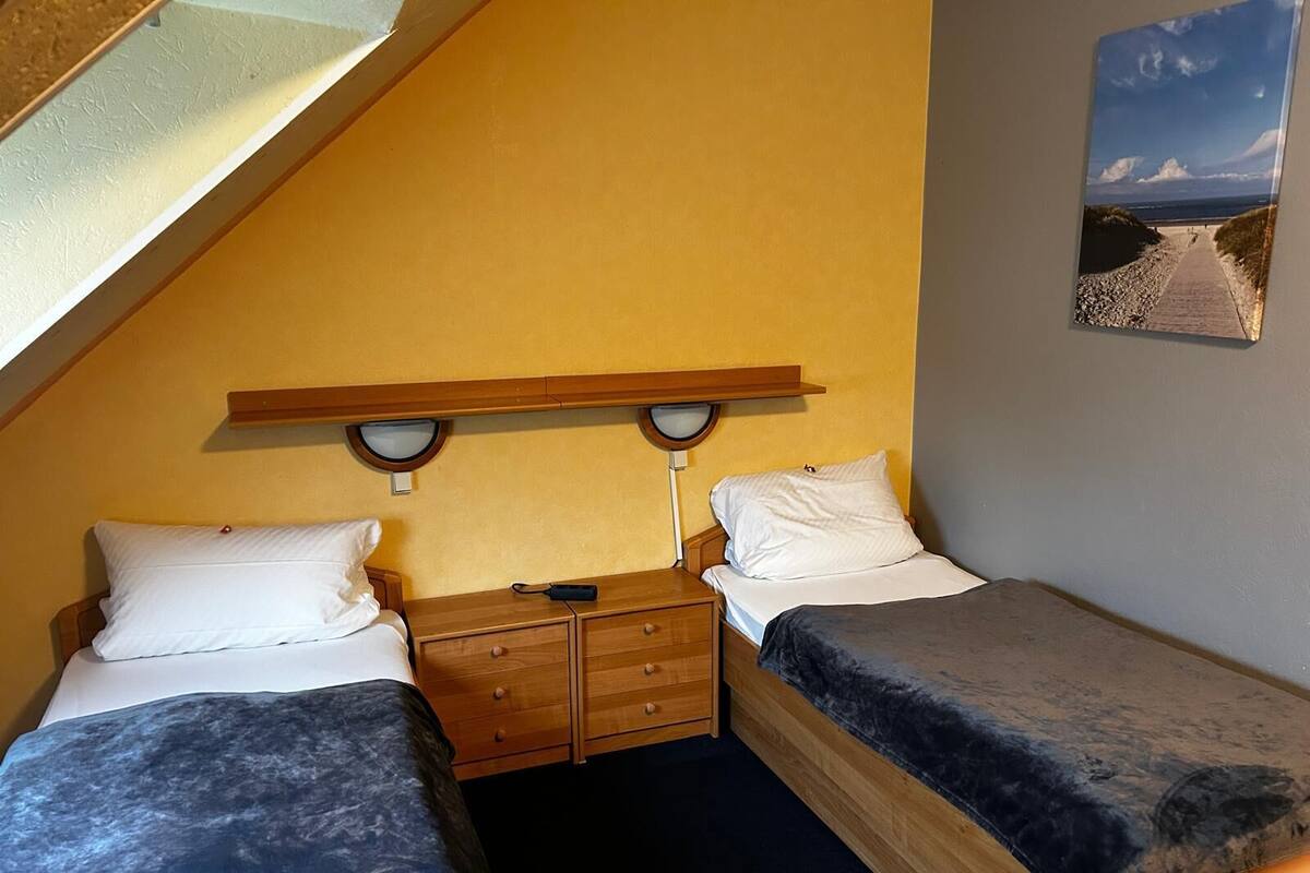Una habitación pequeña y acogedora con dos camas individuales, una mesita de noche de madera y una lámpara fijada a la pared.