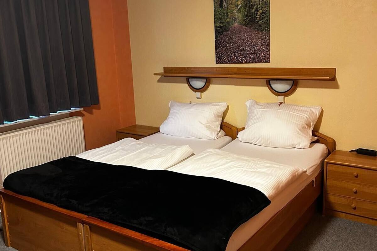 Una cama bien hecha con un edredón negro, cabecera de madera y dos mesitas de noche con lámparas.