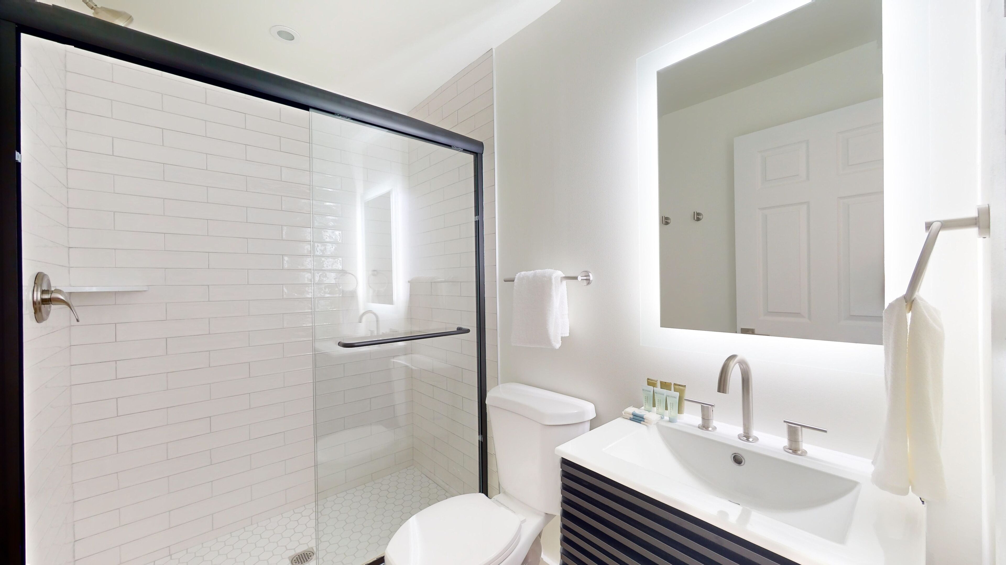 A modern bathroom with a glass shower enclosure, a white toilet, a sink with a mirror, and a towel rack.