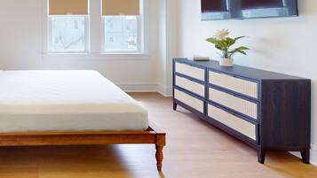 A bedroom with a bed, a dresser, a TV, and two windows with blinds.