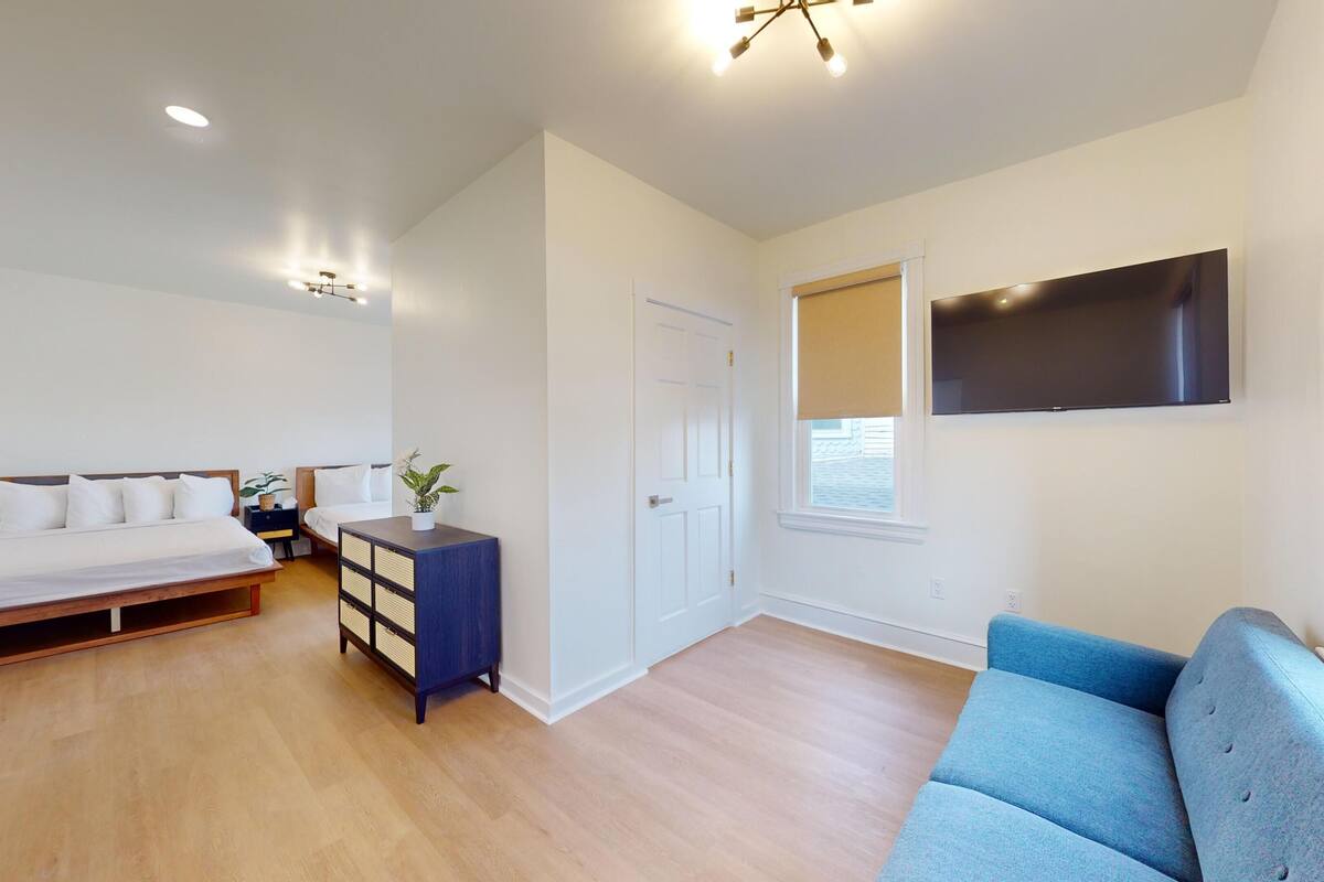 A bedroom with a bed, a dresser, a blue sofa, a TV, and a door.