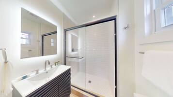 A modern bathroom with a large mirror, a glass shower enclosure, and a white sink.