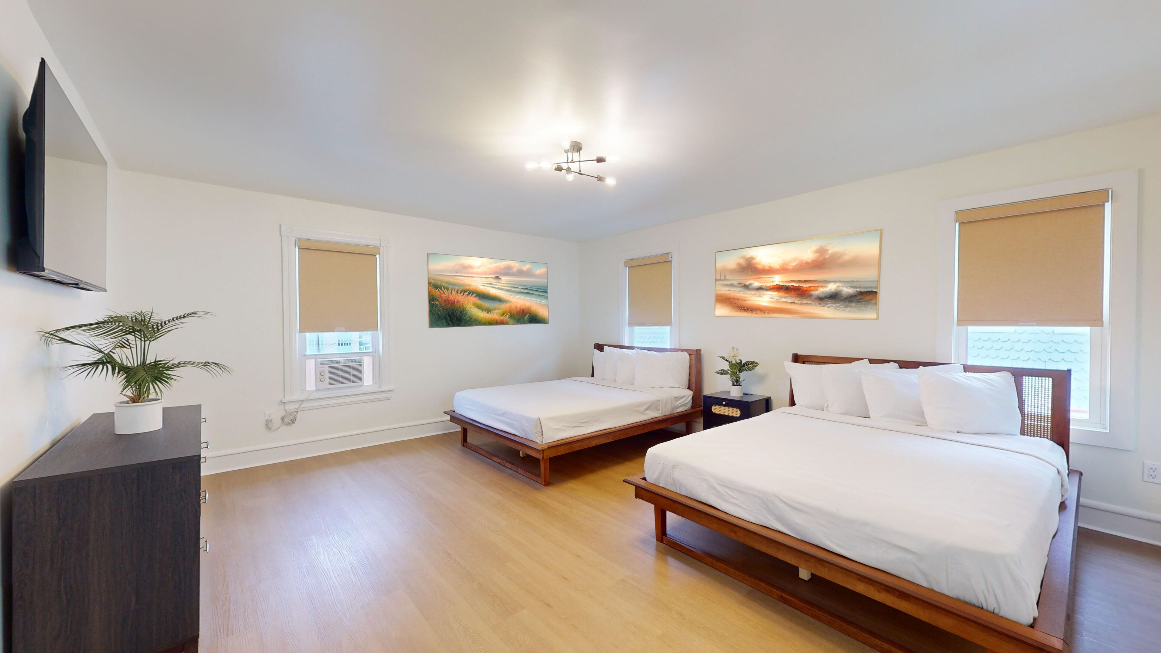 A hotel room with two beds, a TV, a plant, and artwork on the walls.