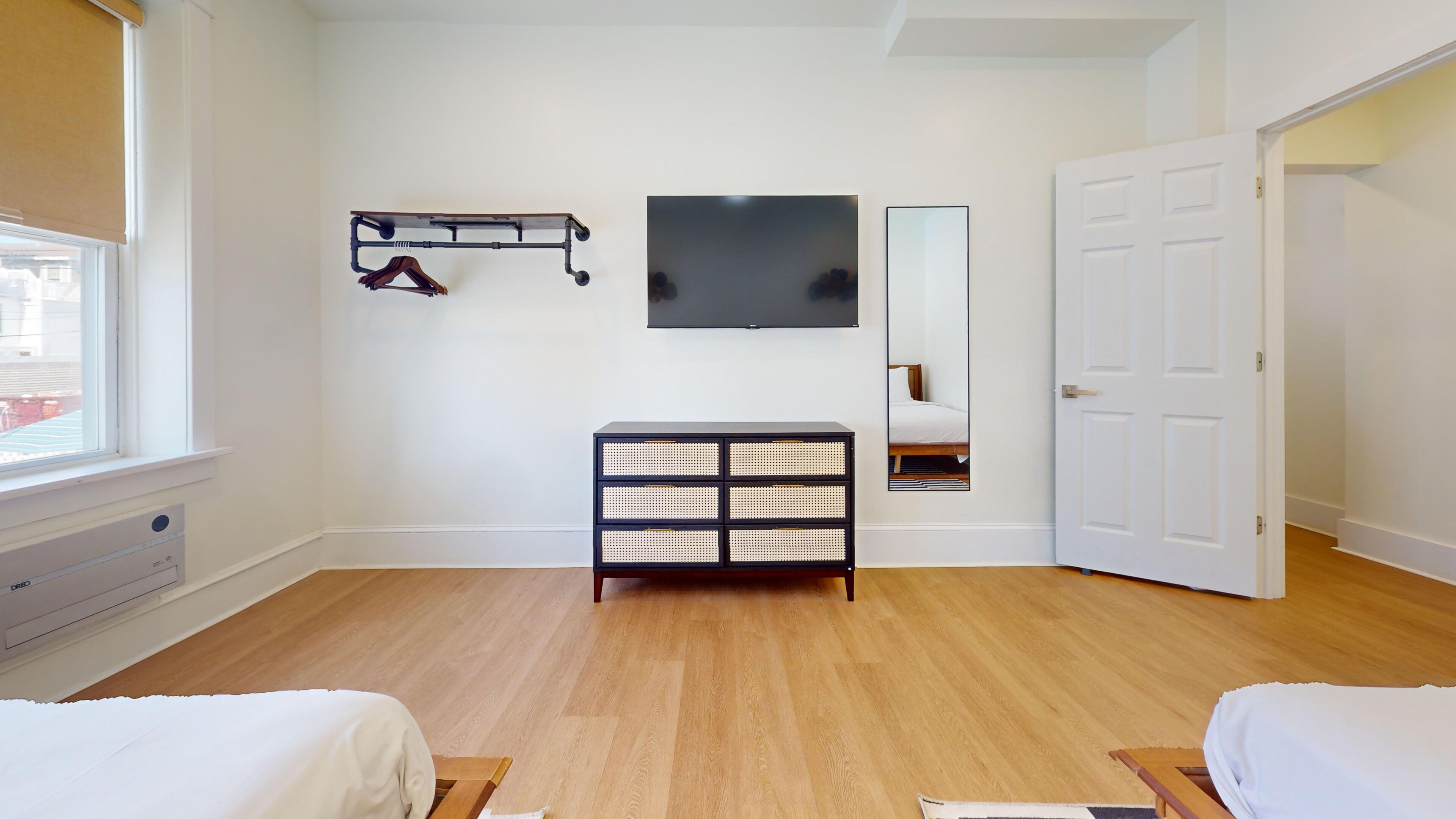 A bedroom with a wooden floor, a black and white storage unit, a bed, a TV, and a door.