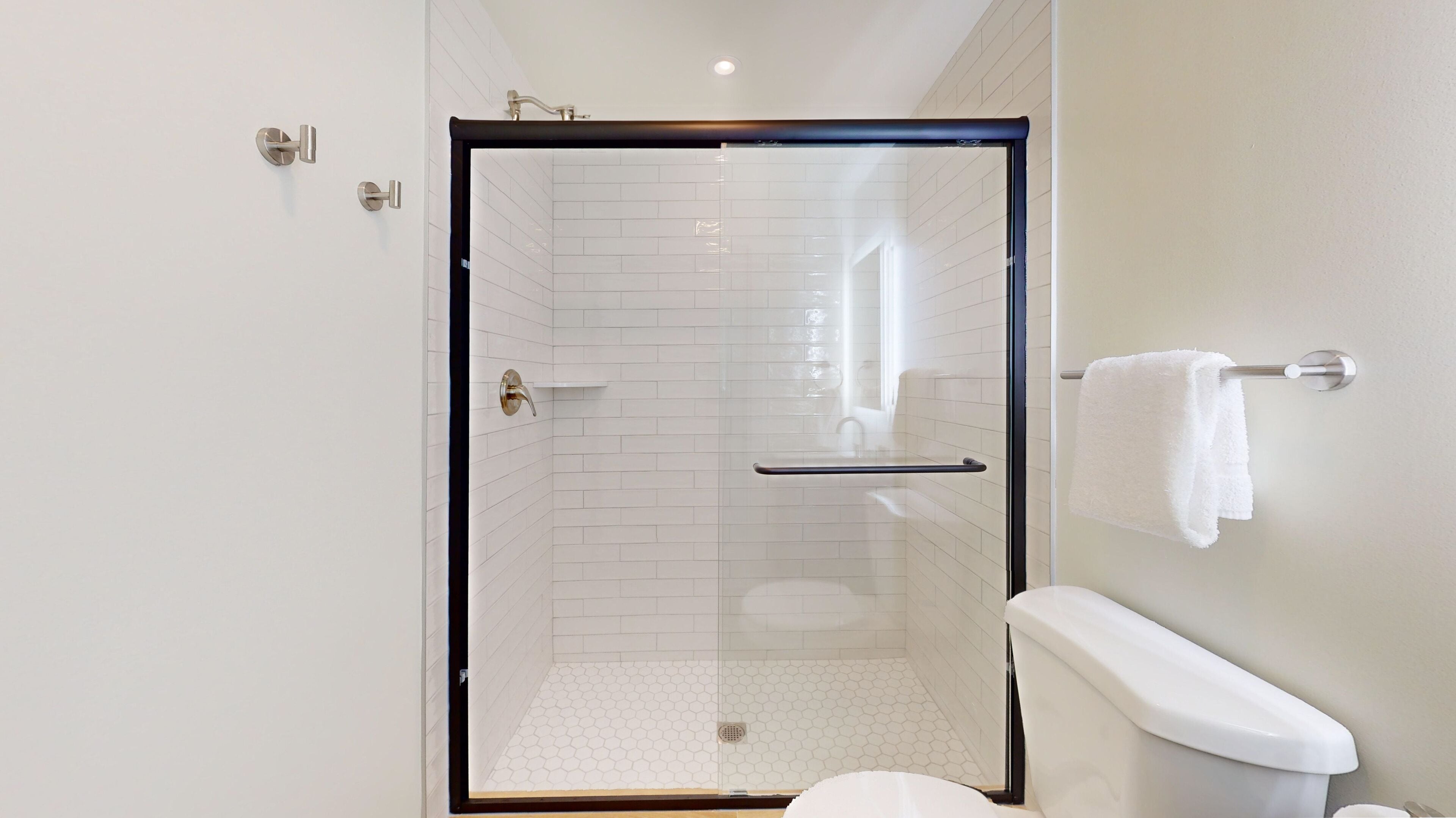 A modern bathroom with a glass-enclosed shower, white tiled walls, and a white toilet.