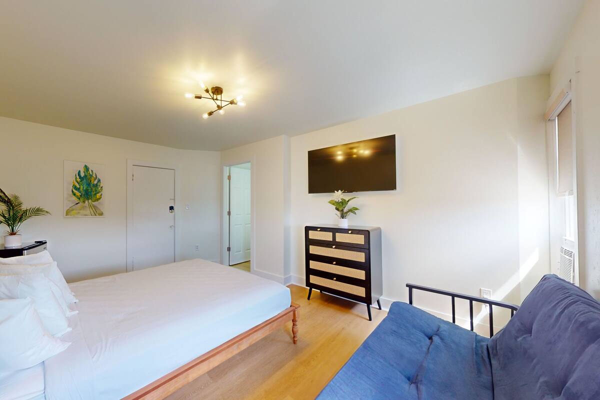 A bedroom with a bed, a dresser, a TV, and a painting on the wall.