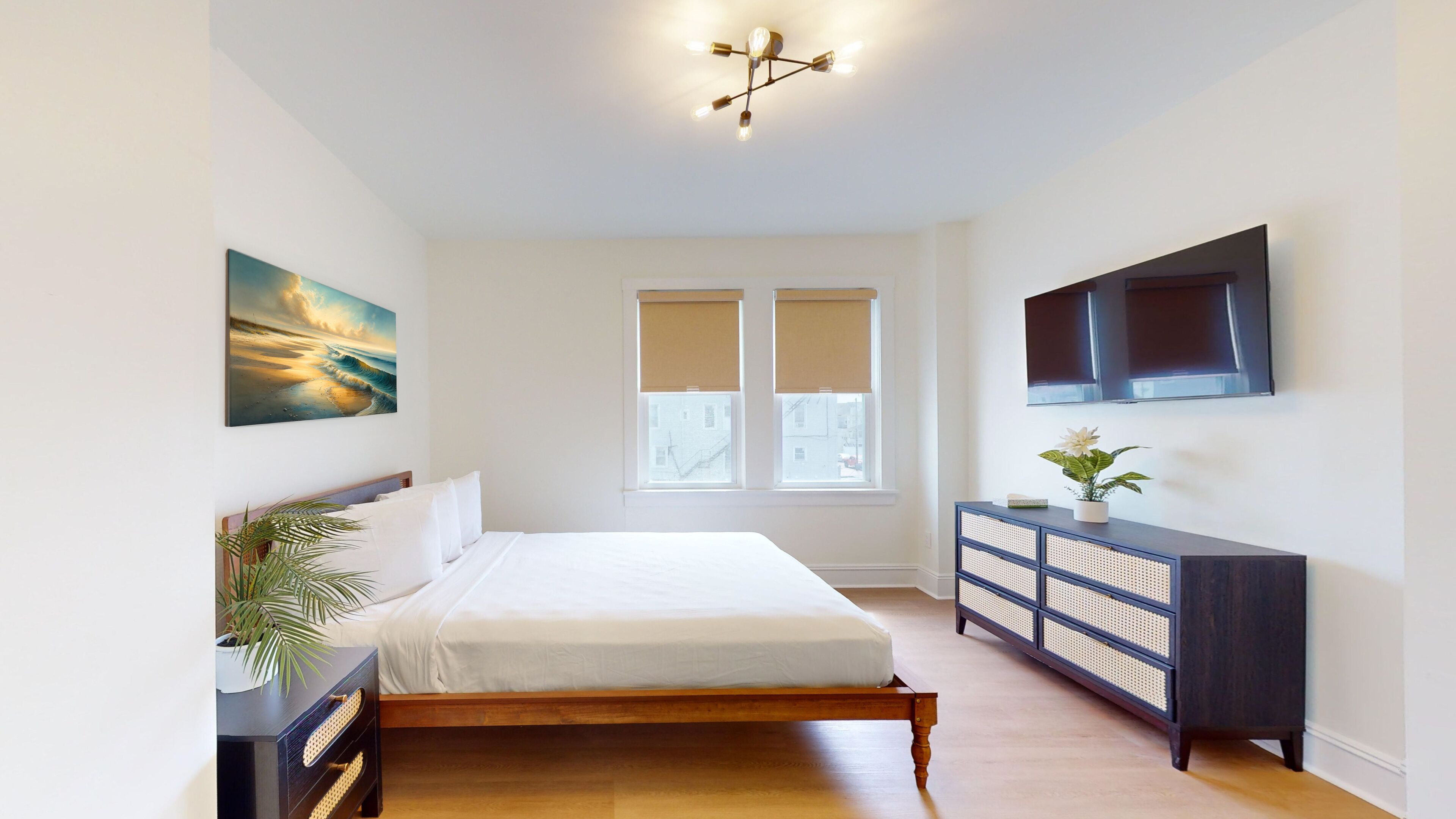 Un dormitorio con una cama, un televisor montado en la pared, una ventana con persianas y un cuadro en la pared.