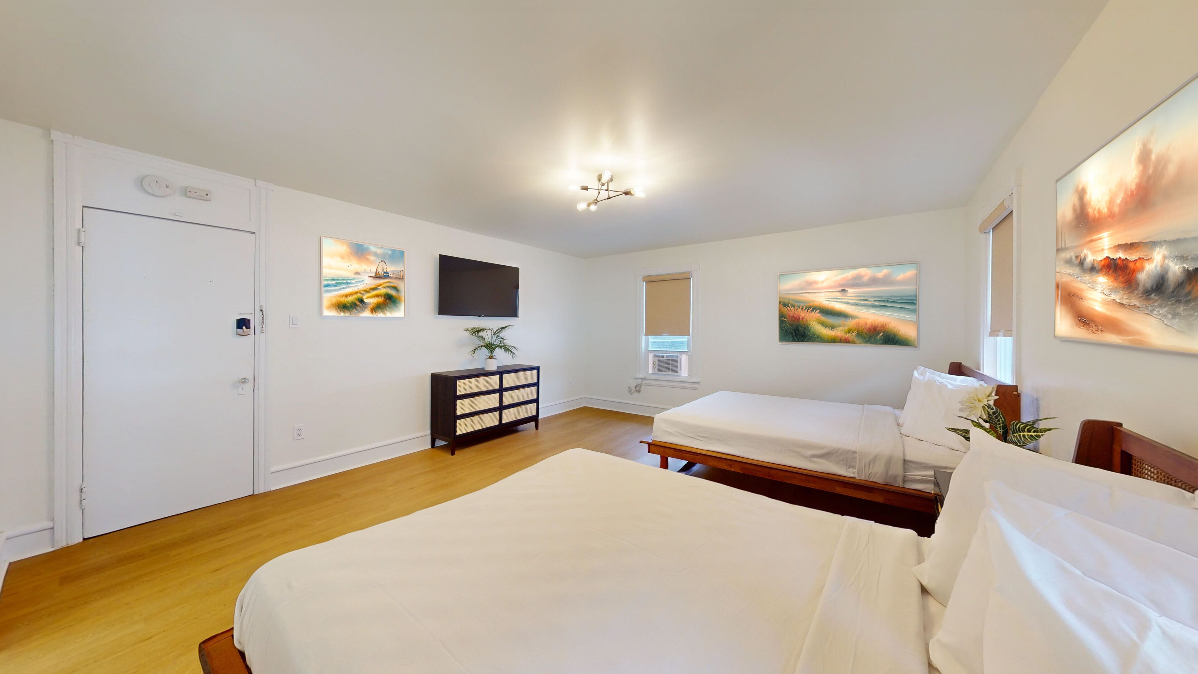 A bedroom with two beds, a TV, artwork, and a window.