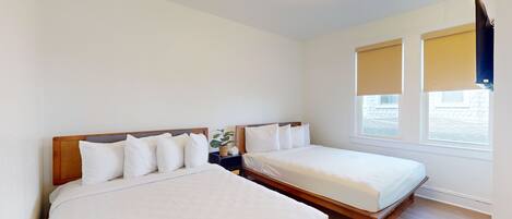 A hotel room with two single beds, a nightstand with a plant, and a window with blinds.
