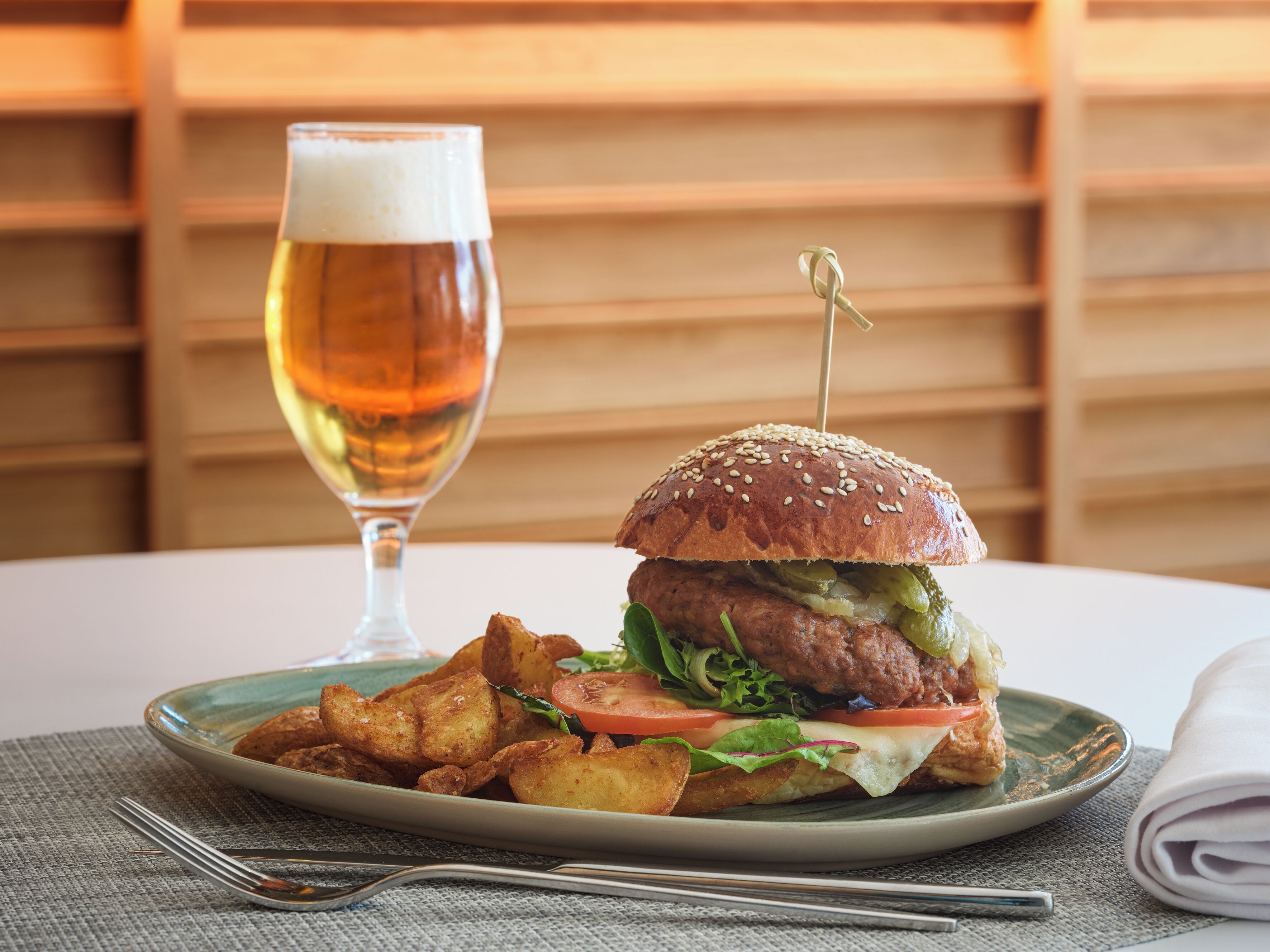 Un plato con una hamburguesa, papas fritas y una jarra de cerveza sobre una mesa.
