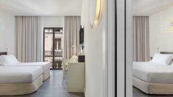 Habitació d'hotel amb dos llits, un escriptori i vista al balcó exterior.