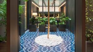 Un hall d’hôtel moderne avec un sol à motifs géométriques, des plantes d’intérieur et une sculpture centrale en bambou.
