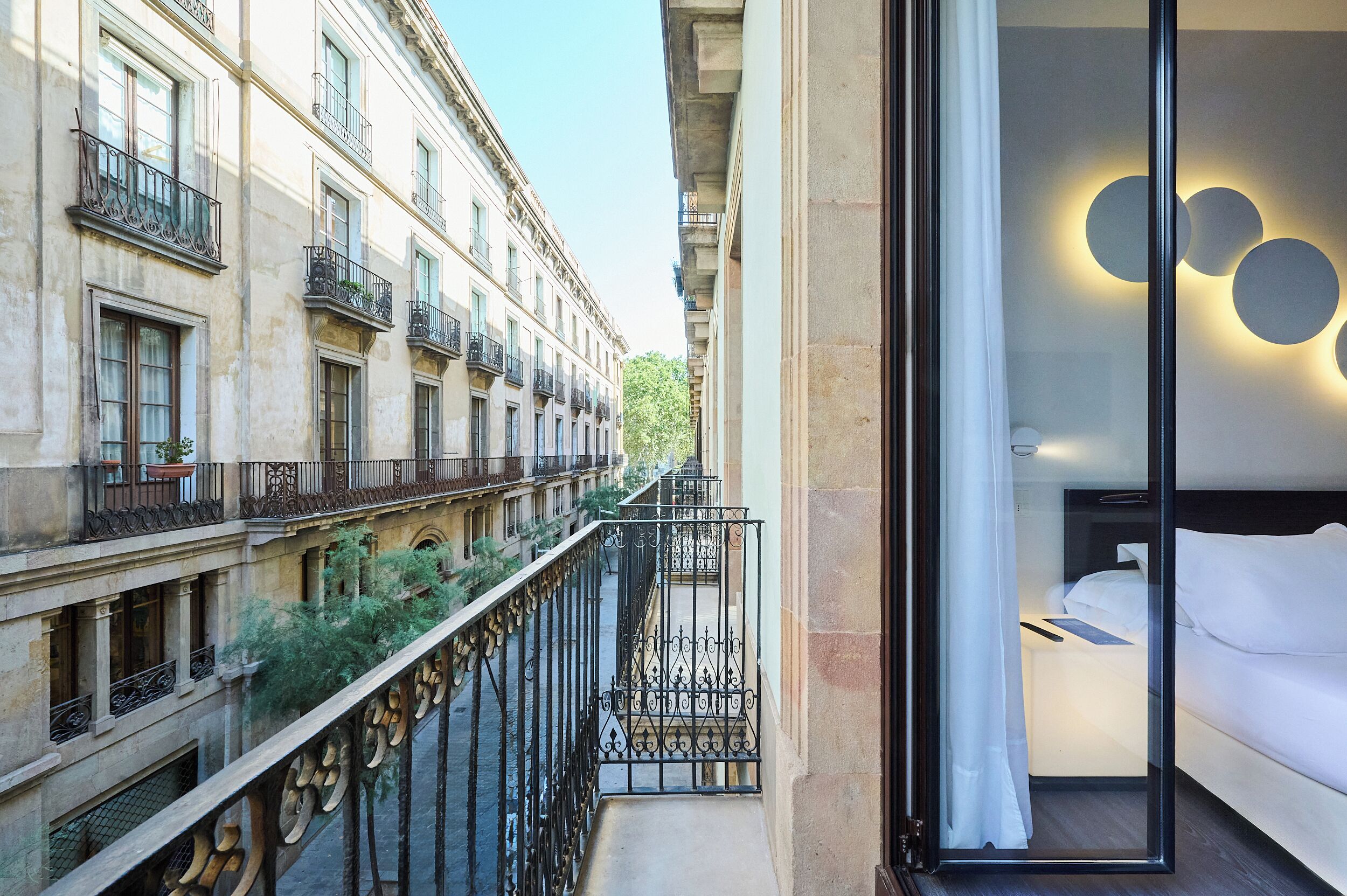 Une chambre d’hôtel avec un balcon donnant sur une rue étroite bordée d’immeubles.