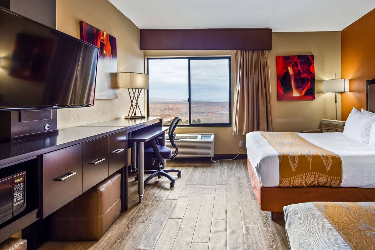 A hotel room with a bed, desk, chair, TV, and large window.