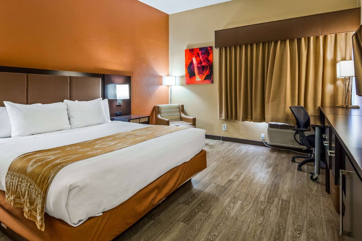 A hotel room with a large bed, a desk with a chair, a lamp, and a painting on the wall.