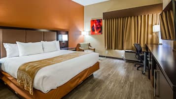 A hotel room with a large bed, a desk with a chair, a lamp, and a painting on the wall.