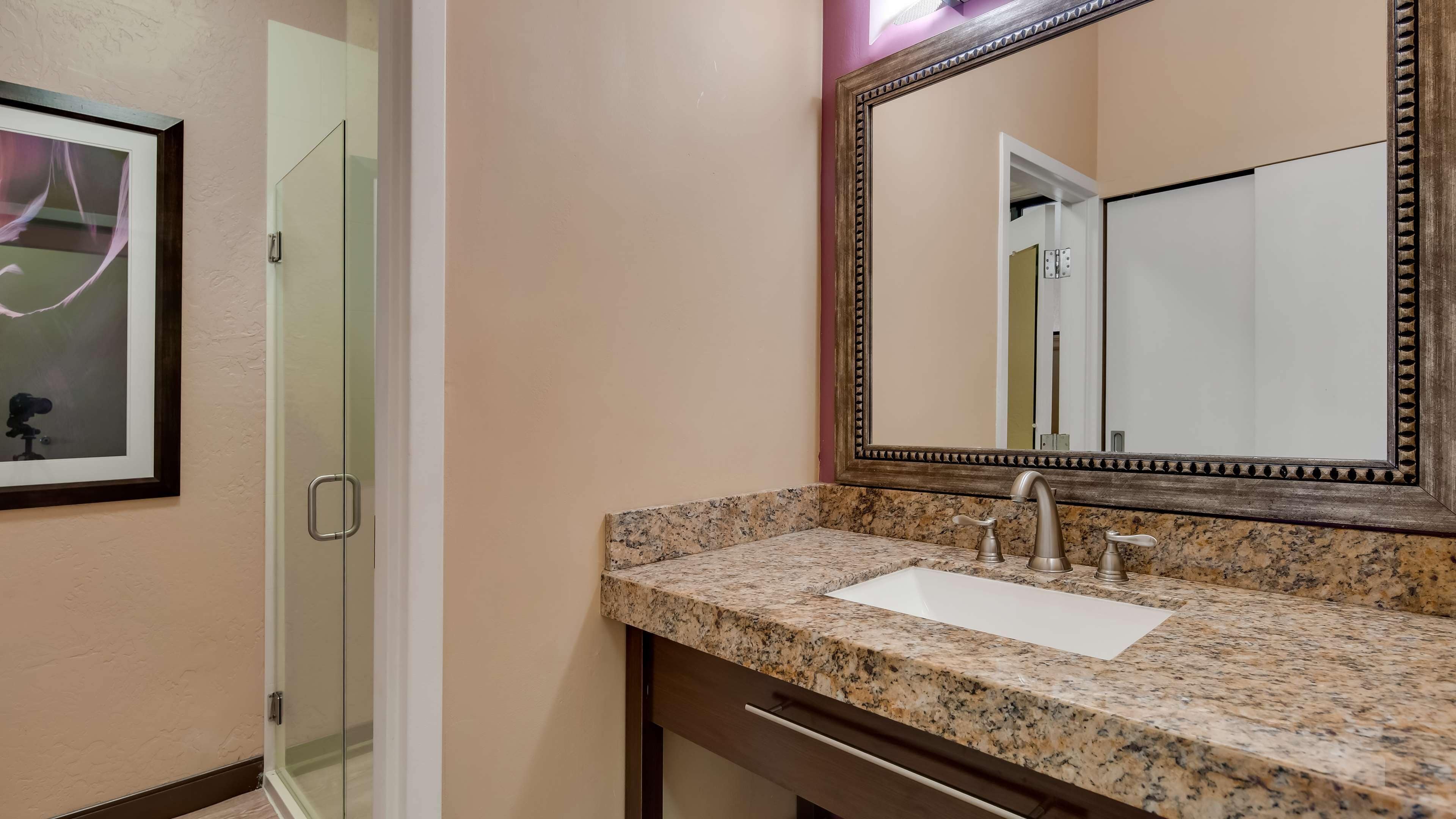 Un baño con encimera de granito, lavabo, espejo y puerta de ducha de vidrio.