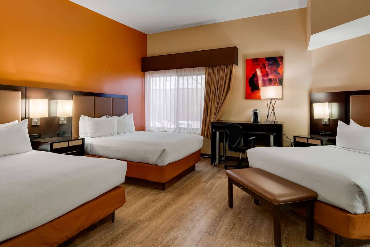 A hotel room with two beds, a desk, a chair, and a bench.