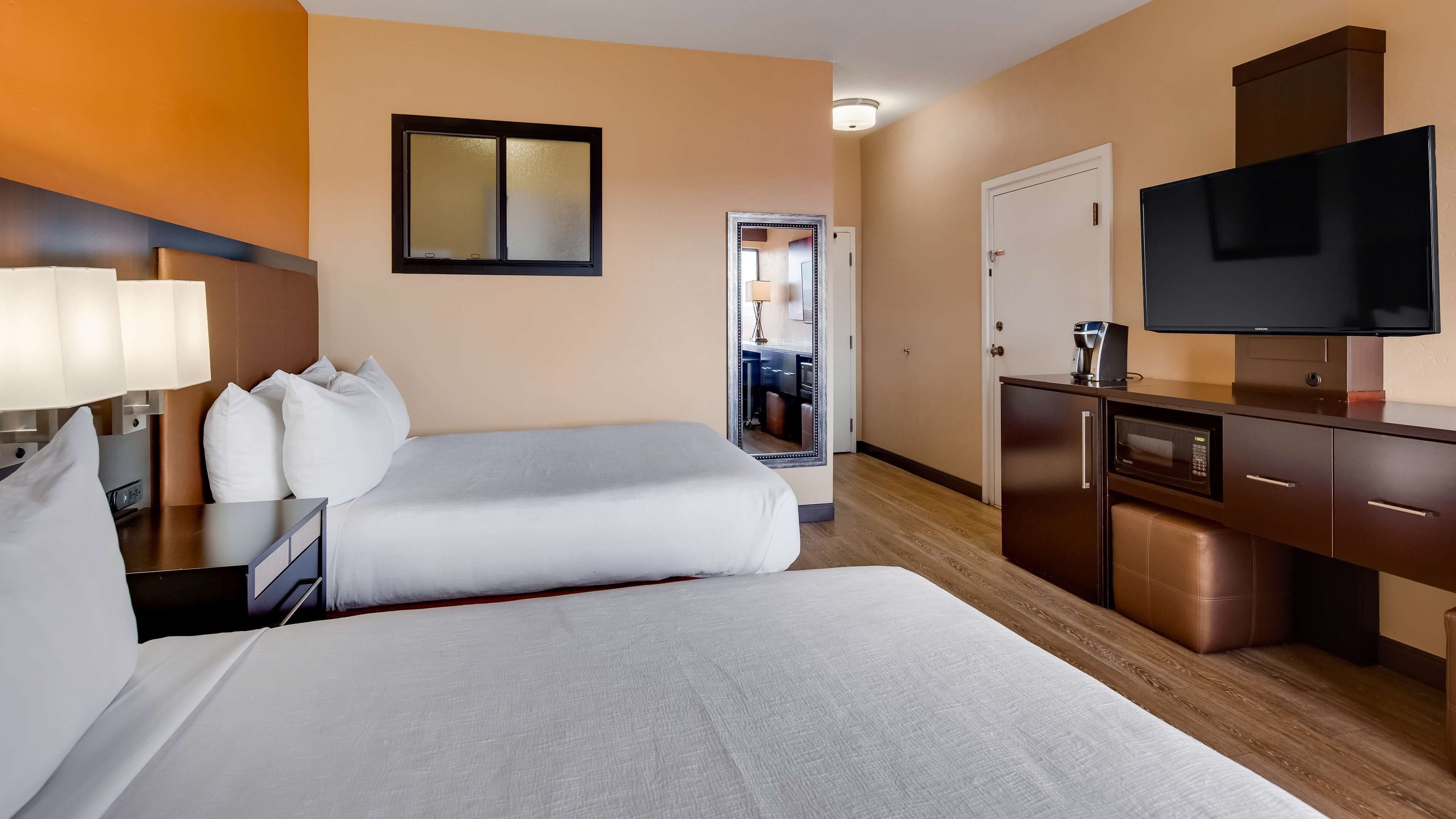 Habitación de hotel con dos camas, televisión, minibar y baño visible a través de una puerta abierta.