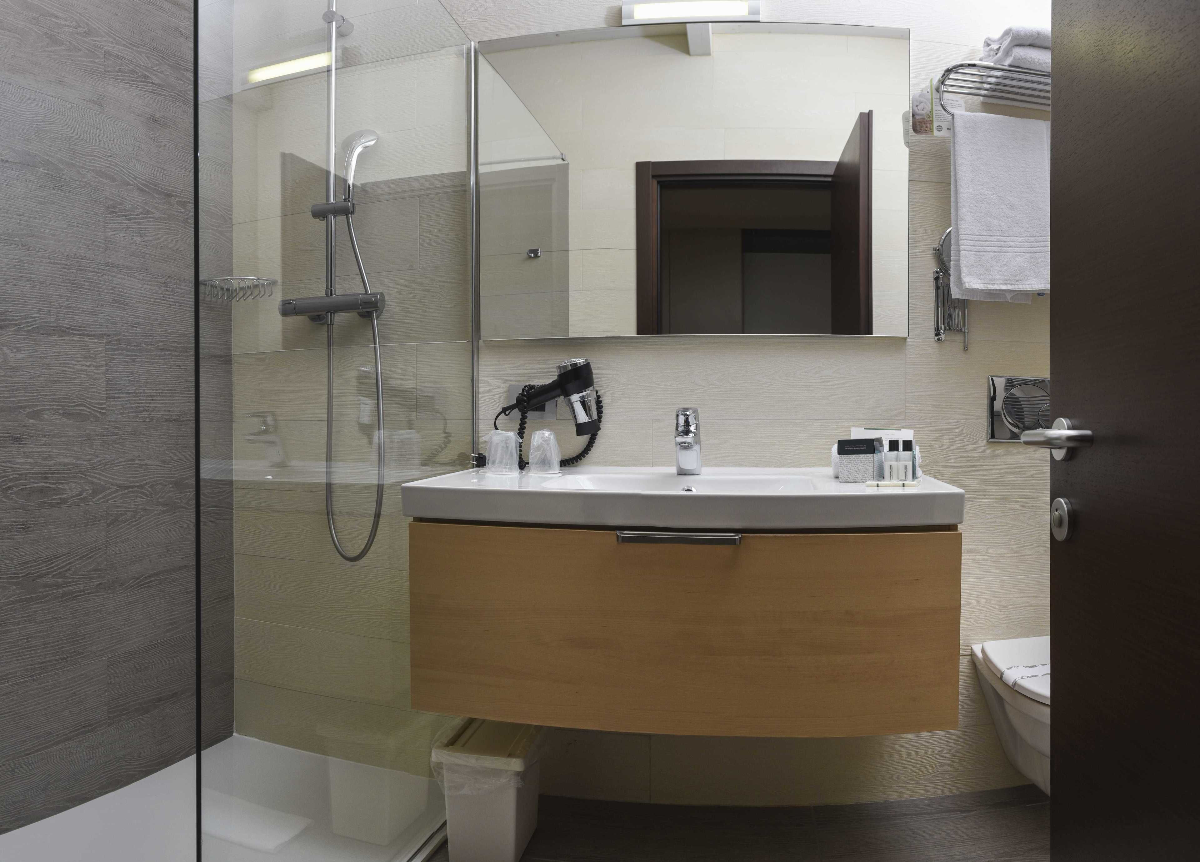 Un baño moderno con cabina de ducha de vidrio, un lavabo blanco con tocador de madera y un espejo sobre el lavabo.
