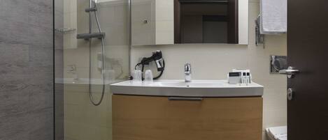 Un baño moderno con cabina de ducha de vidrio, un lavabo blanco con tocador de madera y un espejo sobre el lavabo.
