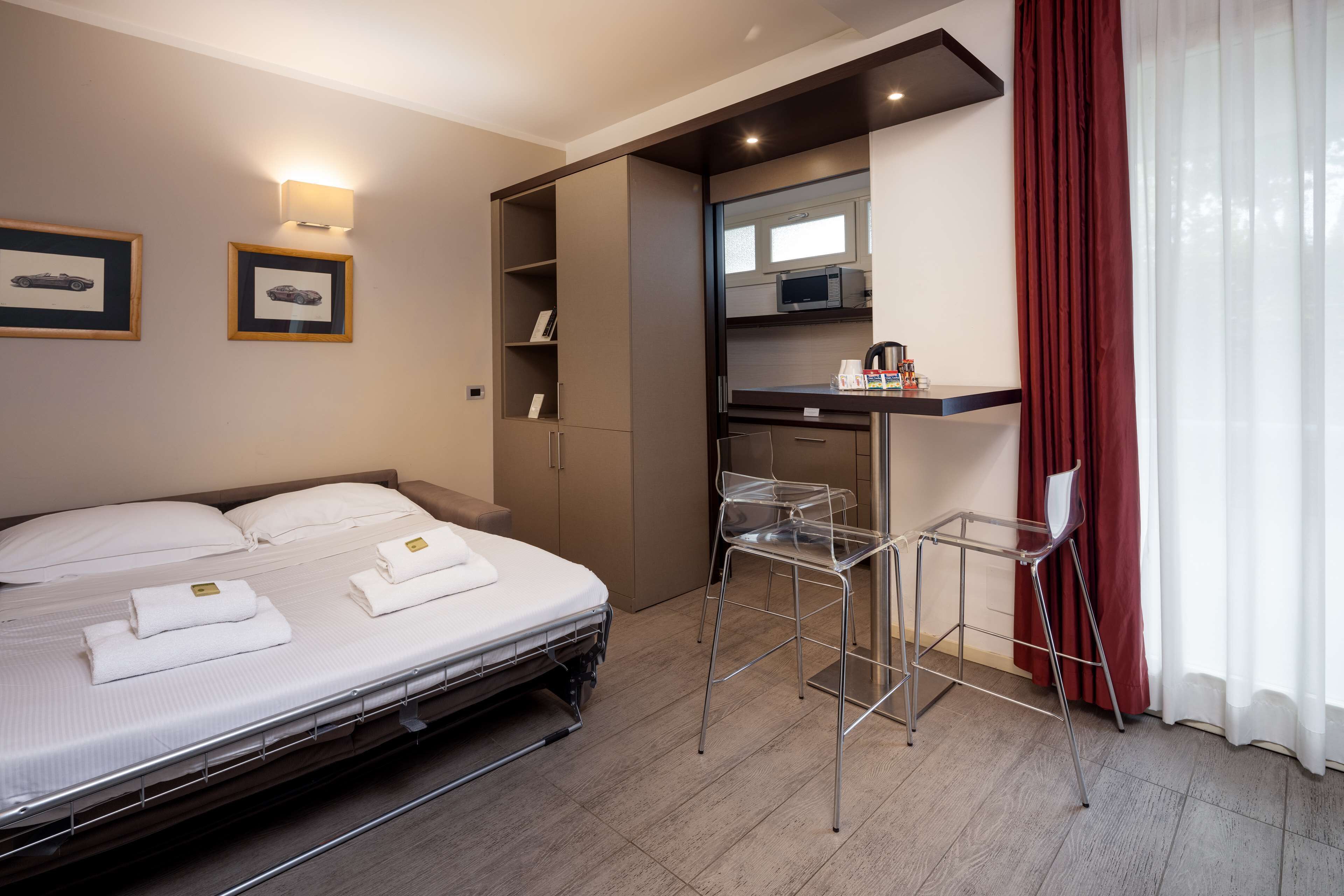 A hotel room with a bed, a desk with a chair, a microwave, and a wardrobe.