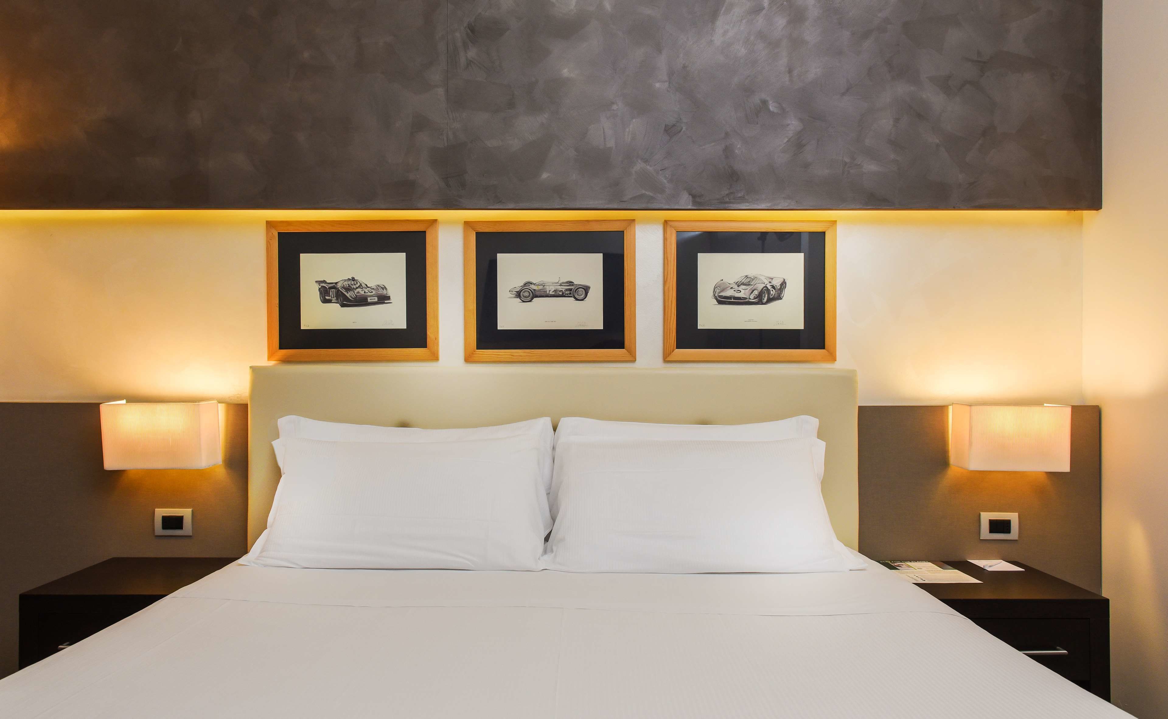 Habitación de hotel con una cama, dos lámparas de noche y tres cuadros en la pared.