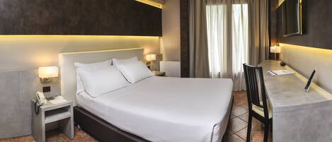 Habitación de hotel moderna con una cama grande, lámparas de noche, un escritorio con silla y un ventanal con cortinas.
