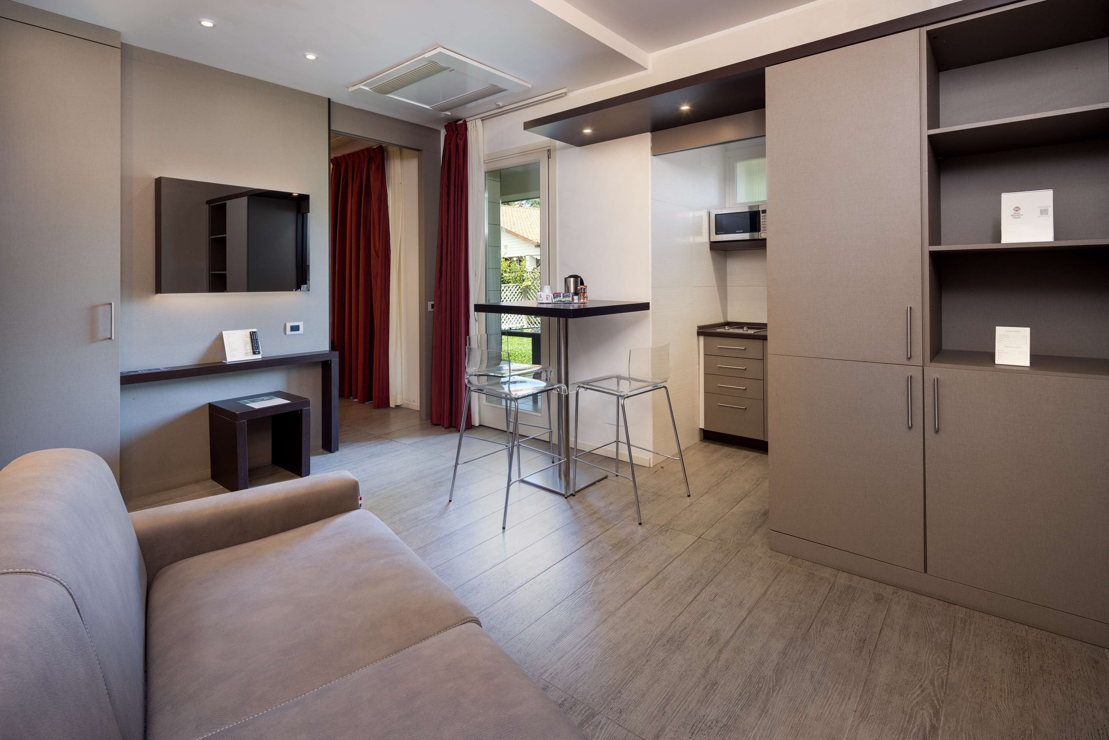 Una sala moderna con sofá, una mesita con sillas, zona de cocina con armarios y puerta corredera que da a un balcón.