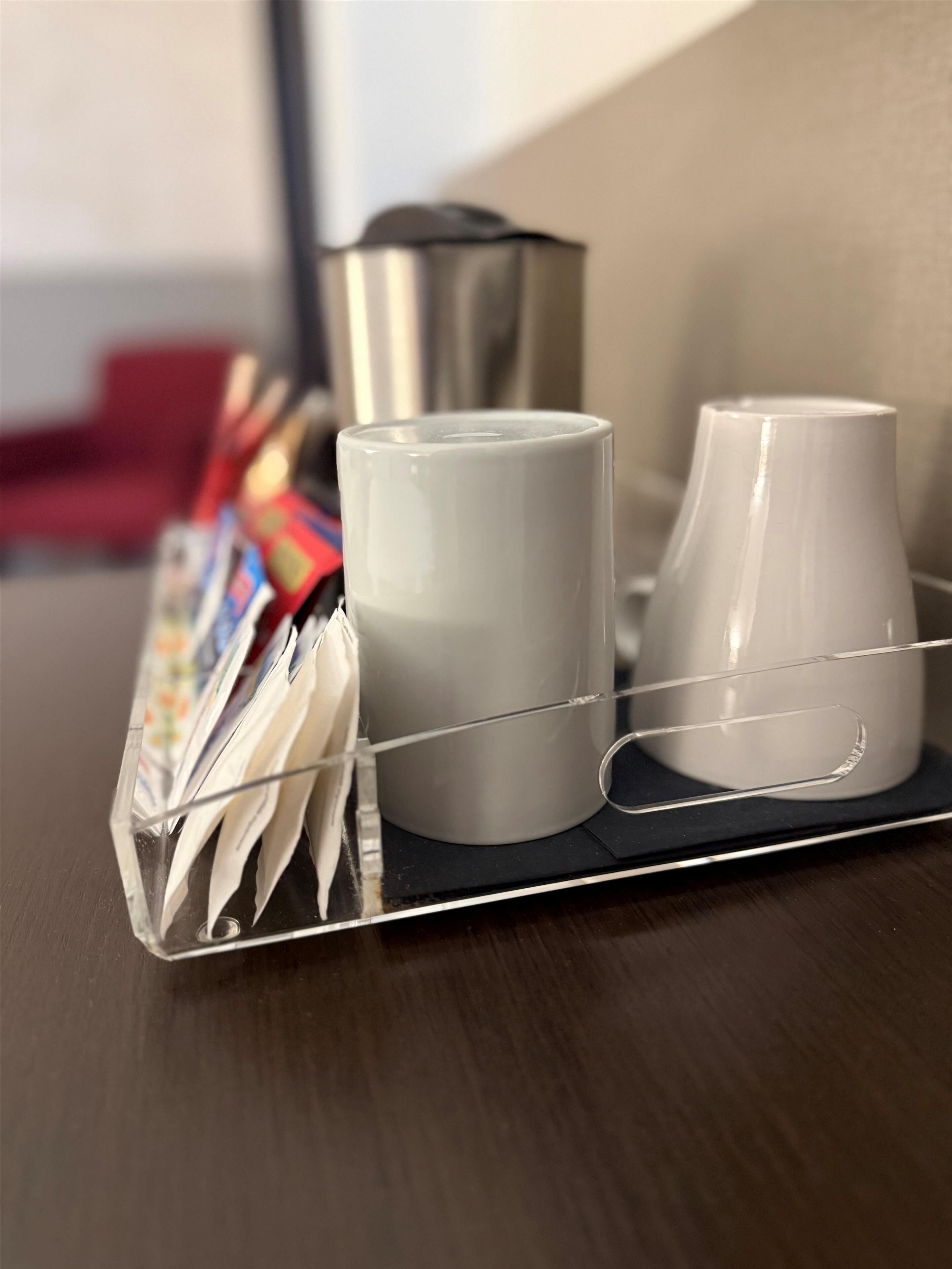 A tray with two white mugs and a stainless steel container on a wooden table.