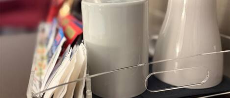 A tray with two white mugs and a stainless steel container on a wooden table.