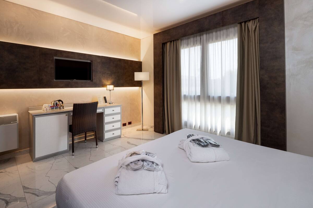 A hotel room with a bed, a desk, a chair, a TV, and a window with curtains.