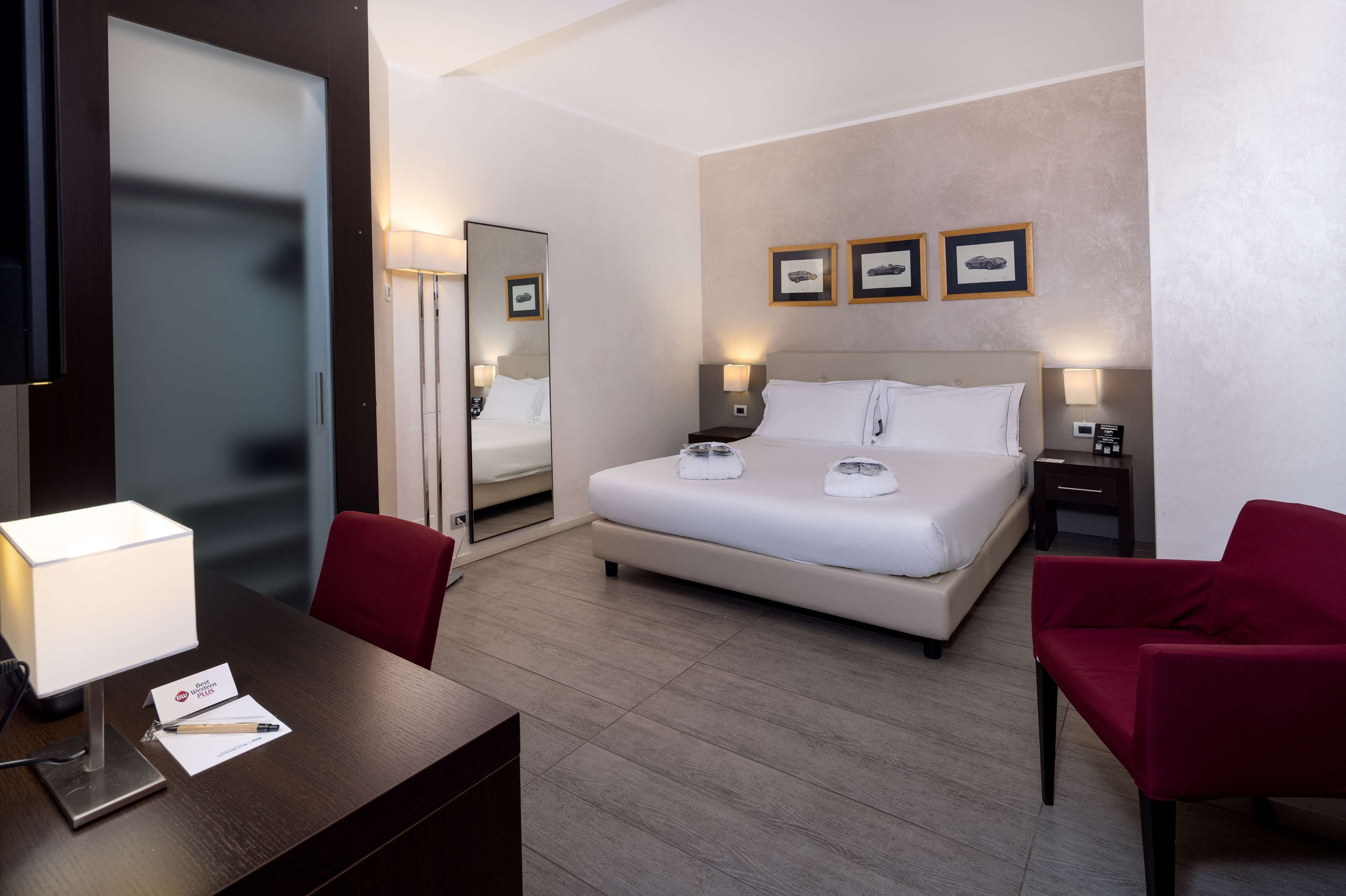 Una habitación de hotel con cama, mesitas de noche, un escritorio con lámpara, una silla y un espejo.