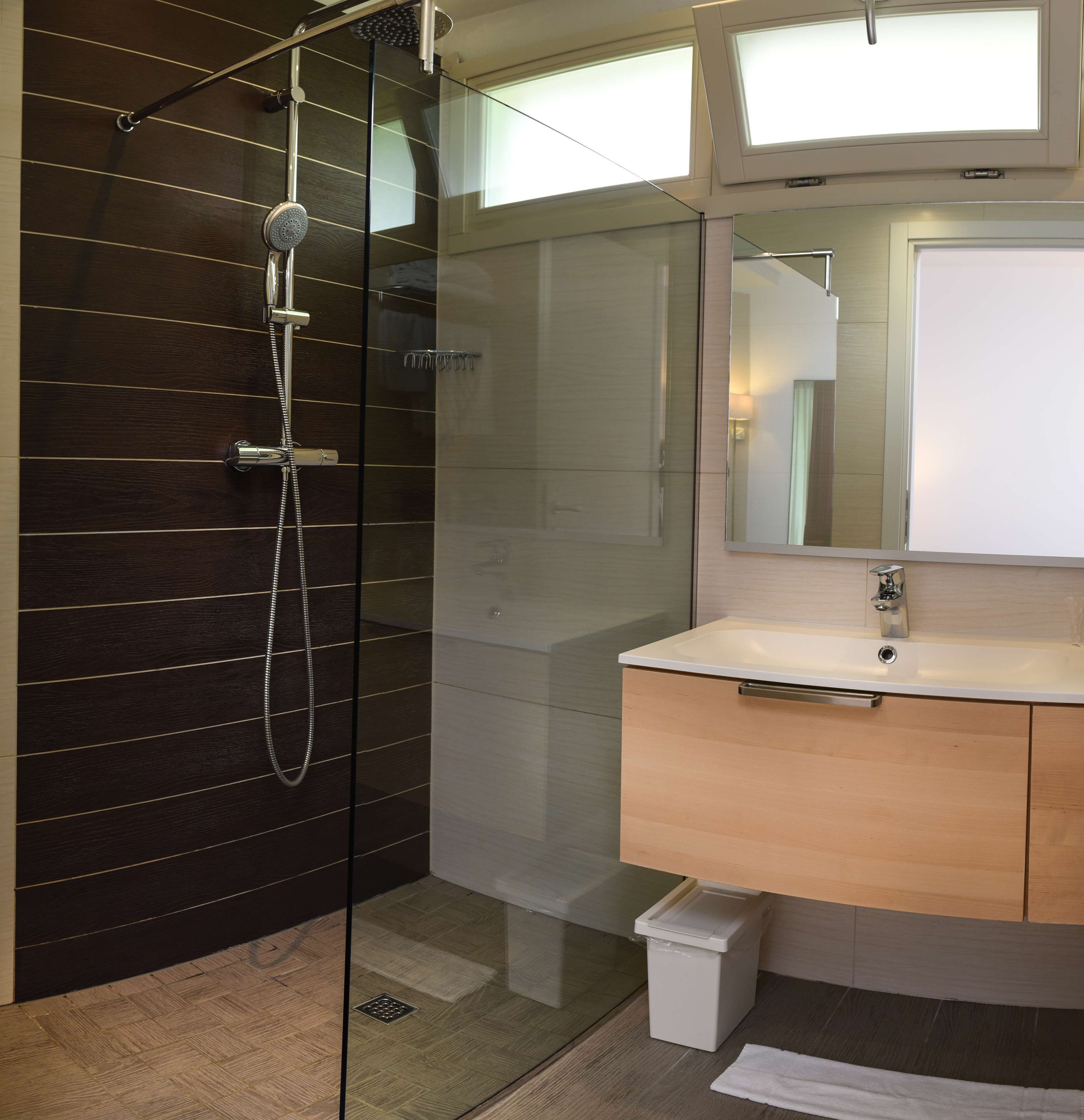 A modern bathroom with a glass-enclosed shower, a wooden vanity, and a large mirror.