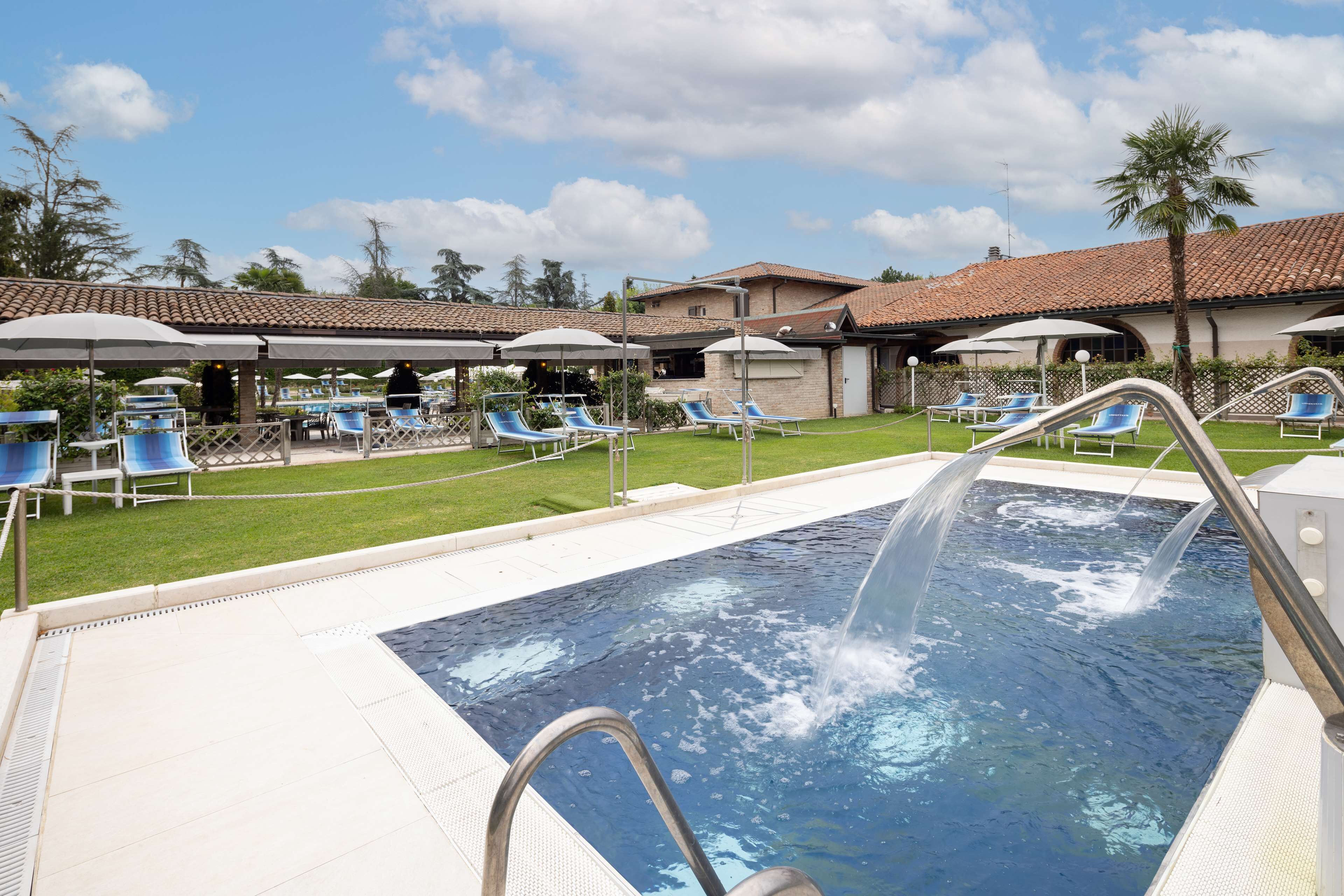 Une piscine entourée de chaises longues et de parasols, elle-même bordée d’une pelouse bien entretenue et d’un bâtiment doté d’un toit en tuiles.