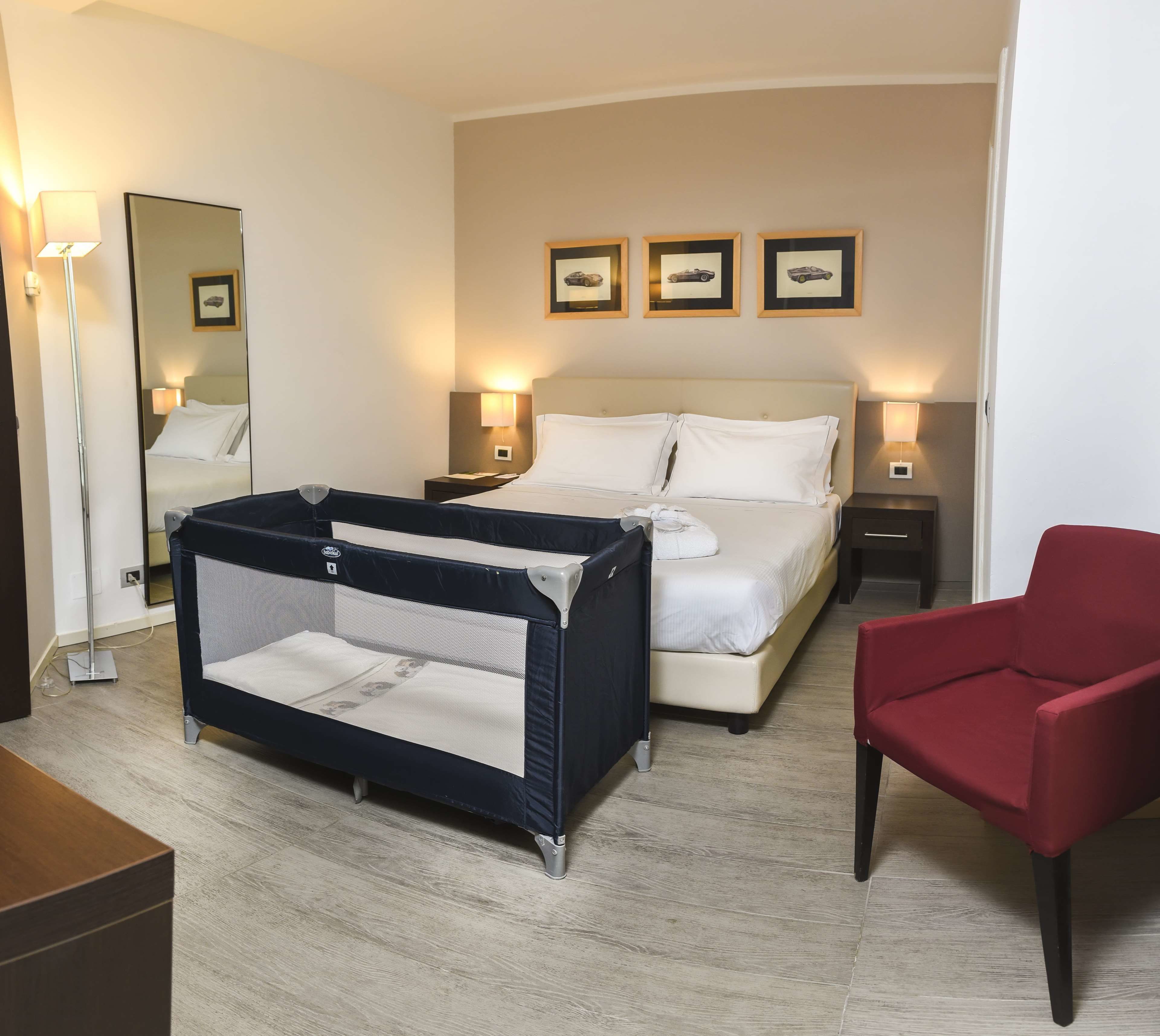 Una habitación de hotel con una cama, una cuna, una silla roja y un espejo.