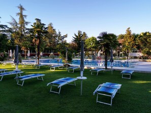 A pool area with multiple lounge chairs and umbrellas, surrounded by lush greenery and trees. - Best Western Plus Hotel Modena Resort (Formigine)